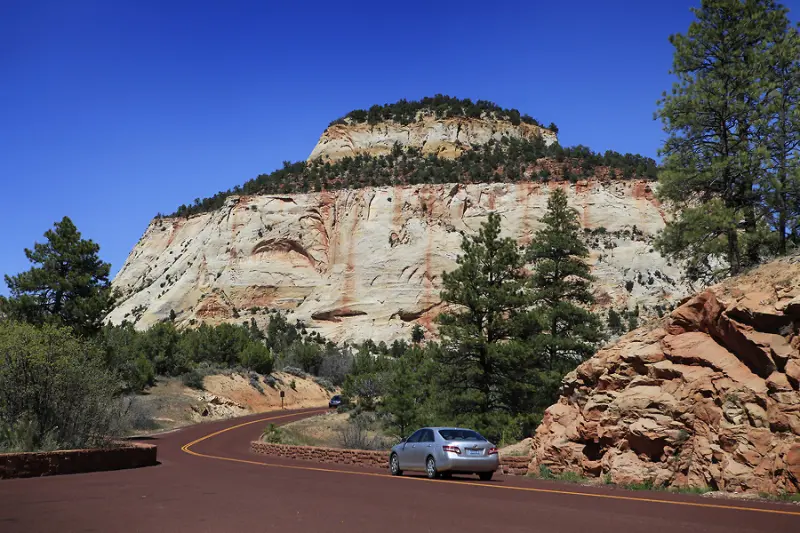 Zion National Park 의 Zion 터널을 거쳐가기 위한 도로이며 도로위에 승용차 한대가 지나가고 있음